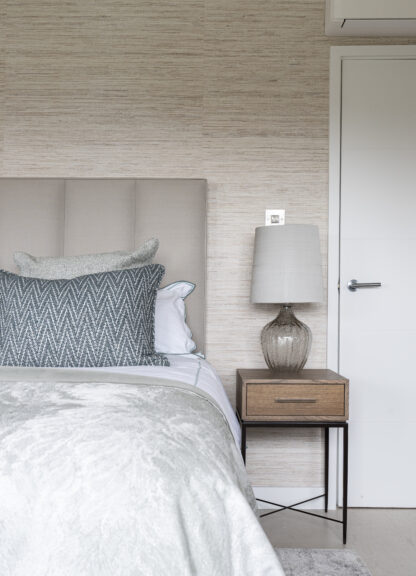 Bedroom detail showing an upholstered headboard, bedside table and table lamp beside a panelled door