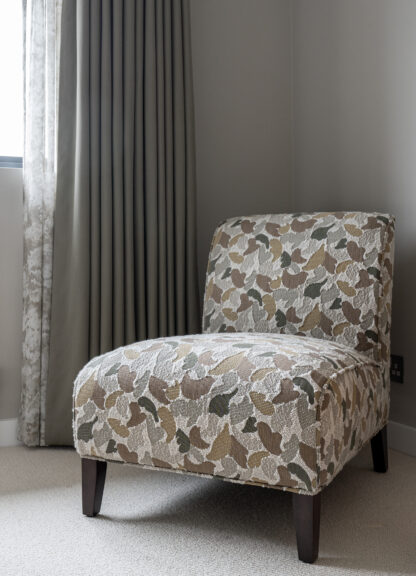 Botanical print accent chair positioned beside floor length patterned curtains