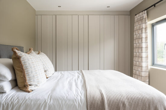 Fitted panelled wardrobes in a neutral bedroom with layered white and stone bedding