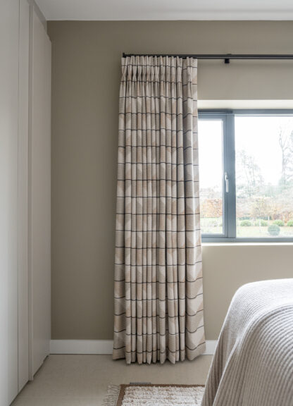 Patterned curtains at a bedroom window with a glimpse of the bed and headboard