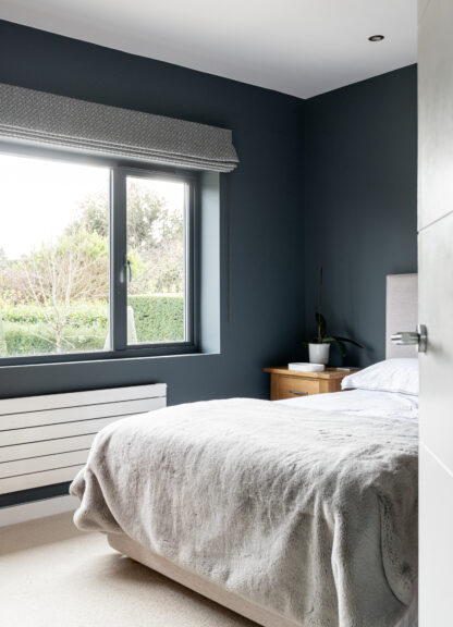 Guest bedroom with a deep navy feature wall, grey bedding and a large window