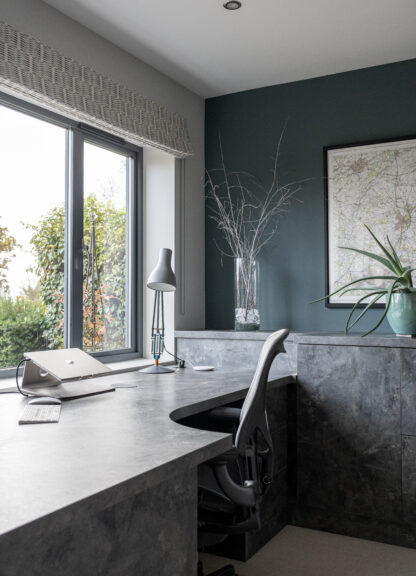 Home office with a navy wall, desk, black task chair and framed artwork
